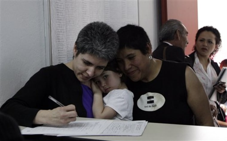 A lesbian couple who gave their first names as Emma, left, and Yanis, right, hold a child as they begin the legal process towards marriage in a city government building in Mexico City, Thursday, March 4, 2010.  Same-sex couples began the new legal process Thursday towards marriage, which will give gay marriages the same status as heterosexual ones. Official marriages are set to begin in the coming weeks.  (AP Photo/Gregory Bull)